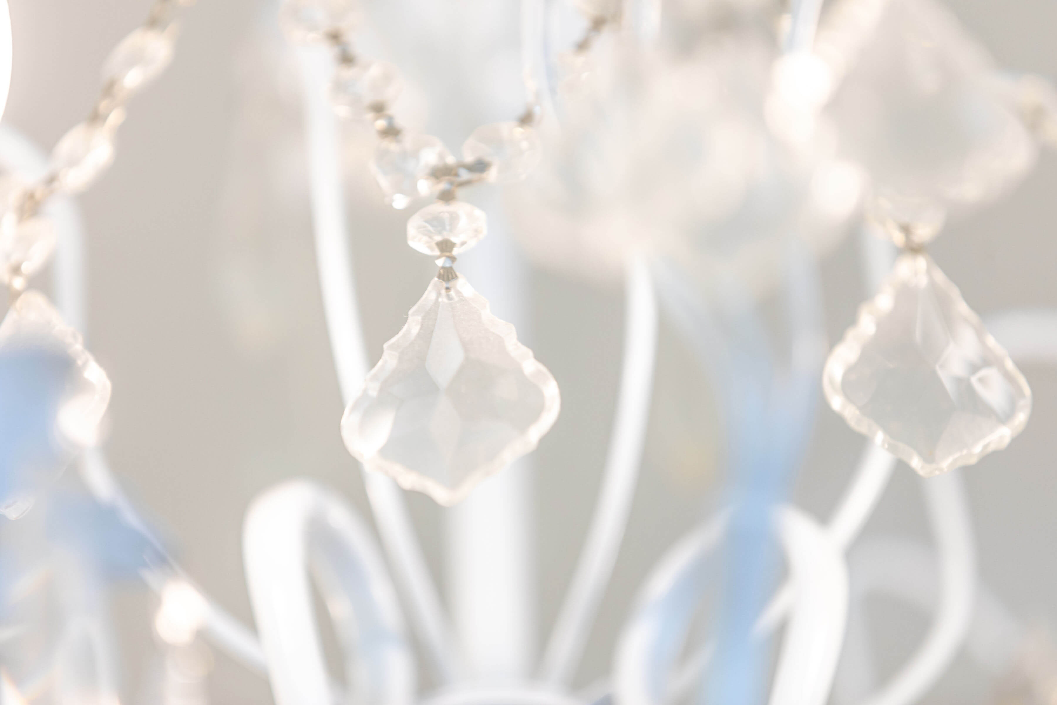 - Salone Estetica in Winchester, MA Close-up of clear, faceted crystal pendants hanging from a white chandelier at the best salon—perfect for clients seeking gorgeous hair color or flawless wedding hair and makeup, set against a softly blurred background. - Salone Estetica in Winchester, MA