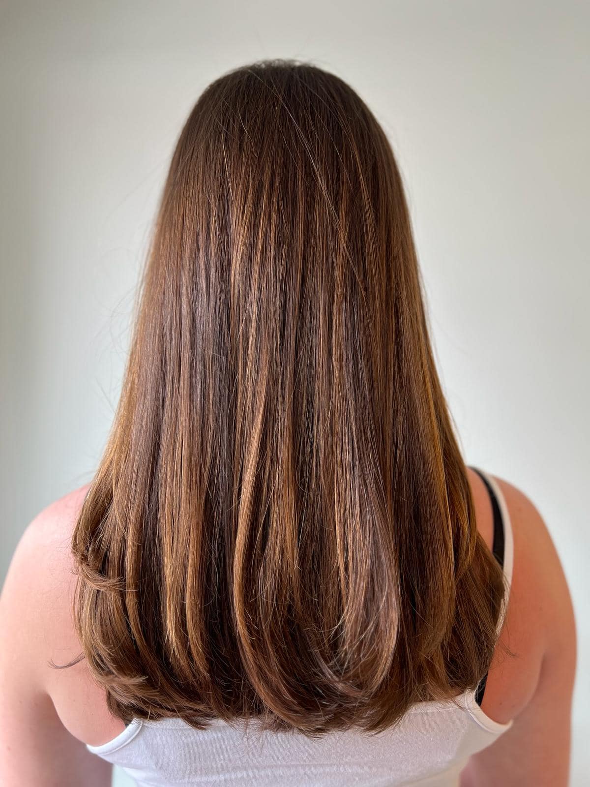 - Salone Estetica in Winchester, MA A person with straight, mid-length brown hair is shown from the back, wearing a white tank top with black straps visible—an inspiring look for those seeking expert wedding hair and makeup by the best salon or talented hair stylist. - Salone Estetica in Winchester, MA