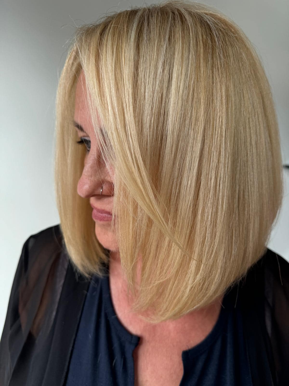 - Salone Estetica in Winchester, MA A person with straight, shoulder-length blonde hair styled in a blunt bob, wearing a black top and a sheer black outer layer, looks slightly to the side—perfect inspiration for wedding hair and makeup. - Salone Estetica in Winchester, MA