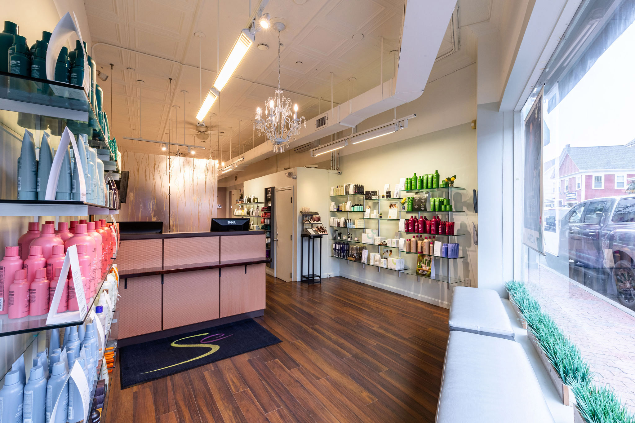 - Salone Estetica in Winchester, MA Modern Aveda salon interior with wood flooring, product shelves along the walls, a reception desk, and a large window facing the street—perfect for your next appointment with an expert hair stylist. - Salone Estetica in Winchester, MA